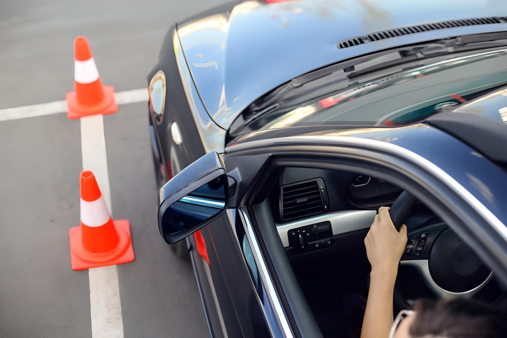 persona conduciendo coche en circuito de practicas con conos naranjas